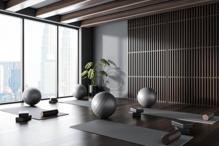 Photo for Dark yoga gym interior with mat and fitball with block and roller, side view hardwood floor. Sport class room with equipment and panoramic window on Kuala Lumpur. 3D rendering - Royalty Free Image