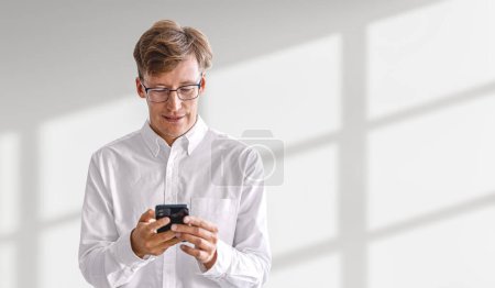 Photo for Smiling businessman typing in phone in hands, empty white shadow background. Online network and social media. Concept of messenger, chat and communication - Royalty Free Image