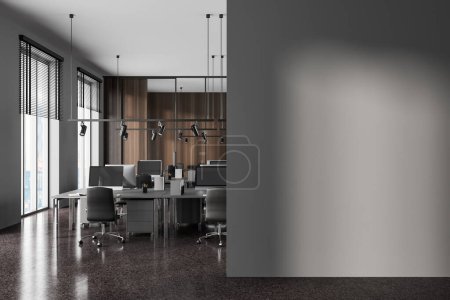 Foto de Interior de la moderna oficina de espacio abierto con paredes de madera gris y oscura, suelo de piedra y filas de mesas de ordenador grises con sillas. Mock up pared a la derecha. renderizado 3d - Imagen libre de derechos