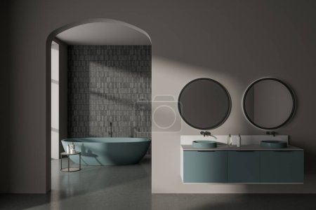 Foto de Interior de elegante cuarto de baño con paredes grises y azulejos, suelo de hormigón, cómoda bañera de color verde oscuro y doble lavabo con dos espejos redondos. renderizado 3d - Imagen libre de derechos