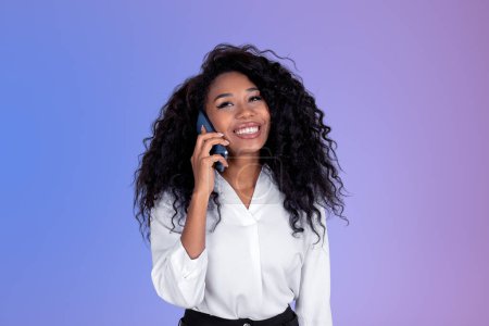 Téléchargez les photos : Femme d'affaires noire souriante parlant au téléphone, portrait de femme africaine sur fond dégradé violet. Concept de communication et médias sociaux - en image libre de droit