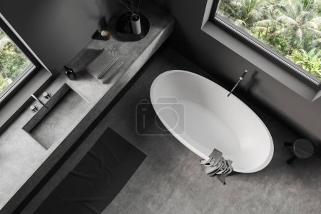 Foto de Vista superior del interior del baño oscuro con lavabo y bañera en la esquina, piso de hormigón gris. Cubierta con accesorios de baño de hotel y ventana panorámica. Renderizado 3D - Imagen libre de derechos