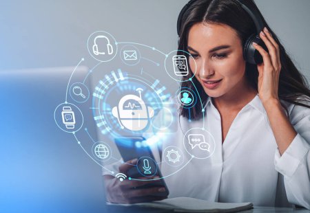 Photo for Businesswoman in headphones is holding smartphone with digital interface with various holograms having online conference call. Robot, smart watch, pie diagram. Office workplace with laptop, notebook - Royalty Free Image