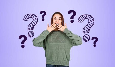 Photo for Portrait of astonished young woman in green sweater with hands near open mouth over purple background with question marks drawn on it. Concept of choice - Royalty Free Image