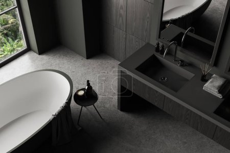 Téléchargez les photos : Vue de dessus de l'intérieur de la salle de bain sombre avec baignoire et lavabo avec miroir, sol en béton gris. Coin bain dans l'appartement de l'hôtel. Fenêtre panoramique sur les tropiques. rendu 3D - en image libre de droit