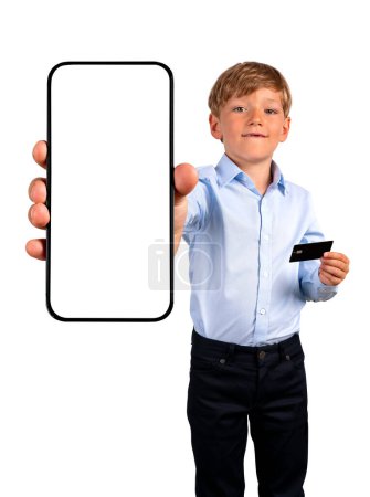 Téléchargez les photos : Enfant garçon montrant un smartphone avec espace de copie écran maquette, tenant une carte de crédit. Isolé sur fond blanc. Concept de paiement en ligne, shopping et application mobile - en image libre de droit