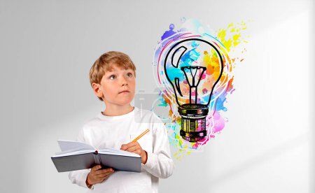 Téléchargez les photos : Un écolier prenant des notes dans un cahier, regardant une ampoule colorée gribouiller sur un mur d'ombre blanc. Concept d'éducation, d'idée, de planification et de démarrage - en image libre de droit