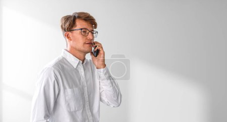 Foto de Empresario en gafas llamando por teléfono, retrato en camisa blanca en la pared de sombra de espacio de copia vacía. Concepto de red empresarial, comunicación en línea y conferencia - Imagen libre de derechos