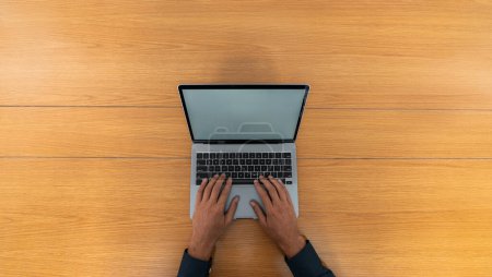 Foto de Vista superior de manos de hombre de negocios escribiendo en el teclado del ordenador portátil en la mesa de madera. Concepto de tecnología y comunicación - Imagen libre de derechos