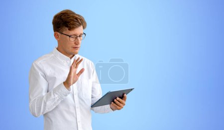 Photo for Businessman in eyeglasses waving hand and using tablet, video call and business meeting, copy space empty blue background. Concept of online conference and connection - Royalty Free Image