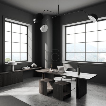 Foto de Interior moderno oscuro de la oficina en casa con ordenador portátil en escritorio de madera, vista lateral minimalista aparador con decoración en piso de hormigón gris. Ventana panorámica en el campo. Renderizado 3D - Imagen libre de derechos