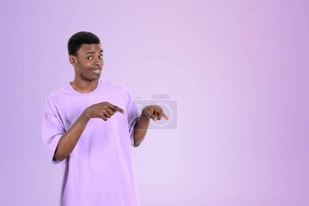 Photo for African American businessman wearing casual wear is standing pointing up with fingers near empty purple wall in background. Concept of model, successful business person, show, presentation - Royalty Free Image