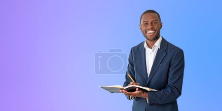 Téléchargez les photos : Portrait de jeune homme d'affaires afro-américain joyeux en costume élégant tenant carnet et stylo et debout près du mur violet. Concept de planification. Espace de copie - en image libre de droit
