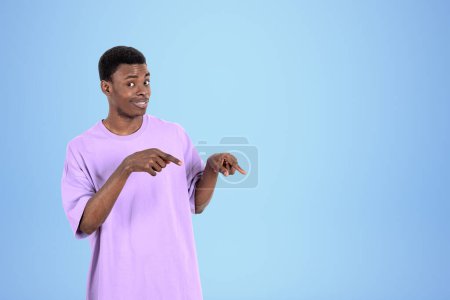 Photo for African American businessman wearing casual wear is standing pointing up with fingers near empty blue wall in background. Concept of model, successful business person, show, presentation - Royalty Free Image