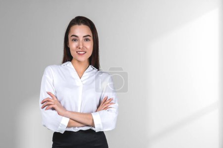 Foto de Sonriente atractiva mujer de negocios que lleva ropa formal está de pie brazos cruzados cerca de la pared blanca vacía en el fondo. Concepto de modelo, persona de negocios exitosa, estudiante, confianza - Imagen libre de derechos
