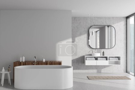 Foto de Interior de baño ligero con bañera y lavabo con espejo, accesorios de baño y toalla de pie en suelo de hormigón gris. Ventana panorámica sobre rascacielos. Mockup pared vacía. Renderizado 3D - Imagen libre de derechos
