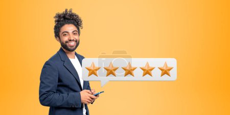 Portrait of cheerful young African American businessman with smartphone giving five star rating. Concept of service ranking. Yellow background