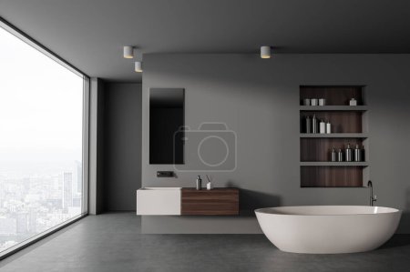Téléchargez les photos : Intérieur de salle de bain élégante avec murs gris, sol en béton, baignoire confortable avec étagères au-dessus et lavabo blanc avec miroir vertical. Rendu 3d - en image libre de droit