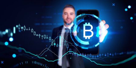 Téléchargez les photos : Homme d'affaires flou montrant smartphone avec symbole Bitcoin et graphiques financiers numériques sur fond bleu foncé. Concept de crypto-monnaie et d'échange décentralisé - en image libre de droit