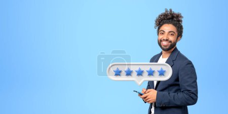 Photo for Portrait of smiling young African American businessman with smartphone giving five star rating. Concept of service ranking. Blue background, copy space - Royalty Free Image