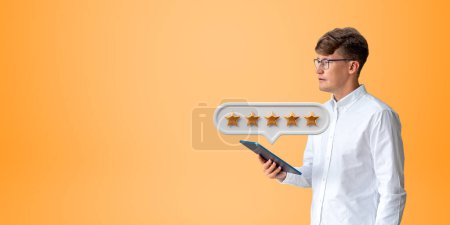 Photo for Portrait of concentrated young European businessman with tablet giving five star rating standing over yellow background. Concept of service ranking and customer feedback. Copy space - Royalty Free Image