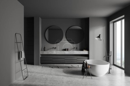 Téléchargez les photos : Intérieur salle de bain sombre avec double lavabo et baignoire, échelle porte-serviettes et lampe au sol en béton gris. Fenêtre panoramique sur campagne. rendu 3D - en image libre de droit