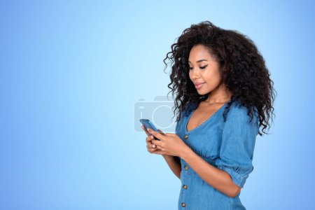 Foto de Mujer africana sonriente escribiendo en el teléfono, retrato en el espacio de copia vacío fondo azul. Concepto de red y comunicación - Imagen libre de derechos