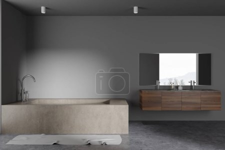 Foto de Interior de elegante cuarto de baño con paredes grises, suelo de hormigón, bañera masiva y doble lavabo de madera con espejo horizontal colgando por encima de ella. renderizado 3d - Imagen libre de derechos
