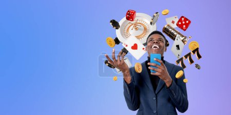Lächelnder junger afroamerikanischer Geschäftsmann mit Smartphone, der im Online-Casino gewinnt, vor violettem Hintergrund mit Roulette, Pokerchips, Würfeln und Karten. Spiel- und Wettkonzept. Kopierraum