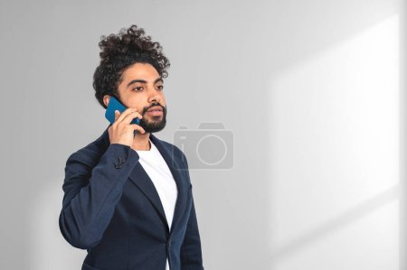 Foto de Retrato árabe de hombre de negocios llamando por teléfono sobre fondo gris claro. Concepto de conferencia en línea y conexión. Copiar espacio - Imagen libre de derechos