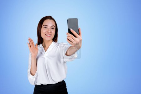 Photo for Businesswoman with phone, smiling and making video call on blue copy space background. Concept of online conference and network - Royalty Free Image