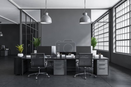 Foto de Interior de negocios oscuro con sillones y ordenador PC en el escritorio, piso de hormigón de baldosas grises. Zona de coworking con ventana panorámica. Mockup pared vacía. Renderizado 3D - Imagen libre de derechos