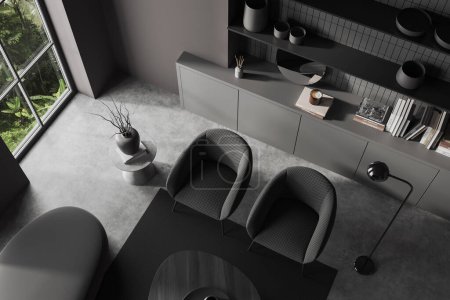 Foto de Vista superior del interior de la sala de estar oscura con dos sillones, cajón y mesa de centro con decoración minimalista, alfombra en piso de hormigón gris. Ventana panorámica de los trópicos. Renderizado 3D - Imagen libre de derechos