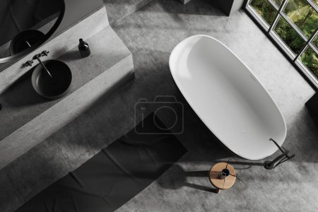 Téléchargez les photos : Vue de dessus de la salle de bain élégante avec des murs gris, sol en béton, baignoire confortable debout près de la fenêtre et lavabo gris avec miroir rond. Rendu 3d - en image libre de droit