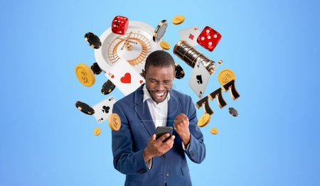 Fröhlicher junger afroamerikanischer Geschäftsmann mit Smartphone, der im Online-Casino gewinnt, vor blauem Hintergrund mit Roulette, Pokerchips, Würfeln und Karten. Spiel- und Wettkonzept