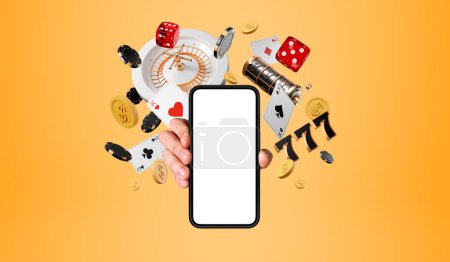Man hand showing a smartphone mock up blank screen, roulette and casino poker cards with money falling on orange background. Concept of online game, mobile app and gambling