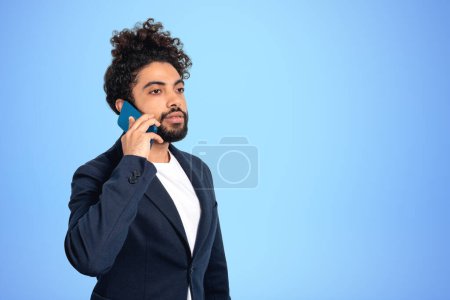 Foto de Retrato de hombre de negocios de Oriente Medio llamando por teléfono sobre fondo azul. Concepto de conferencia y red en línea. Copiar espacio - Imagen libre de derechos