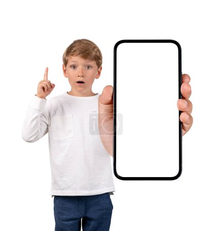 Foto de Niño con mirada sorprendida, el dedo hacia arriba, mostrando el teléfono con pantalla de copia simulada espacio, aislado sobre fondo blanco. Concepto de idea y aplicación móvil - Imagen libre de derechos