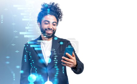Foto de Oriente Medio sonriente hombre de negocios con teléfono inteligente en la mano, holograma bursátil. Hud financiero digital con gráfico de barras y candelabro. Concepto de comercio y éxito. Copiar espacio - Imagen libre de derechos