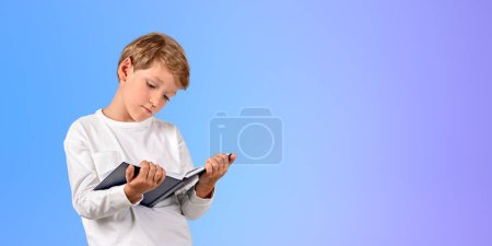 Téléchargez les photos : Enfant concentré avec livre dans les mains, lisant attentivement le portrait sur fond dégradé d'espace de copie. Concept d'éducation, d'apprentissage en ligne, de cours et de connaissances - en image libre de droit