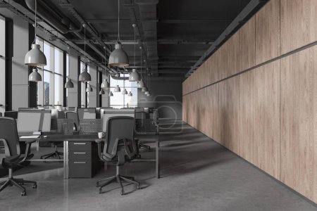 Foto de Interior de oficina oscuro con sillones y ordenadores PC en la mesa en fila, pared de madera y suelo de hormigón gris. Loft de empresa de espacio abierto con ventana panorámica en Nueva York. Renderizado 3D - Imagen libre de derechos