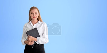 Photo for Young business woman with notebook and pen in hands, smiling portrait looking at the camera on copy space empty blue background. Concept of business education and student - Royalty Free Image
