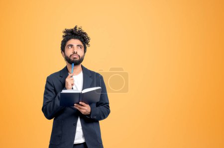 Foto de Hombre de negocios árabe pensativo con cuaderno, pluma a barbilla con mirada reflexiva, espacio de copia de fondo naranja vacío. Concepto de creación de empresas - Imagen libre de derechos