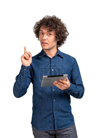 Photo for Young man in casual denim shirt, holding a tablet in hand and finger pointing up. Isolated over white background. Concept of plan, idea, offer and recommend - Royalty Free Image
