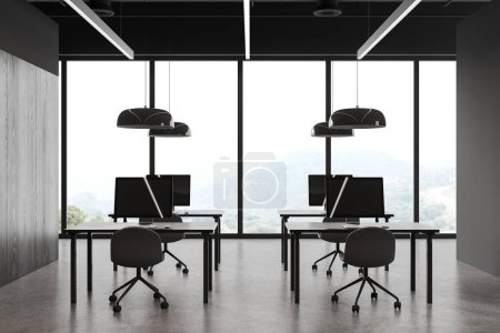 Foto de Interior de espacio de trabajo oscuro con sillas y ordenador PC en el escritorio en fila, piso de hormigón gris. Oficina de negocios y ventana panorámica con vistas al campo. Renderizado 3D - Imagen libre de derechos