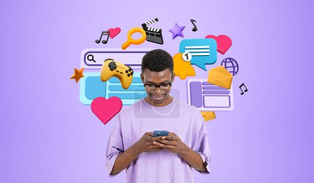 Foto de Joven hombre africano alegre en ropa casual de pie con teléfono cerca de la pared púrpura con coloridas redes sociales e iconos de entretenimiento en línea. Streaming aplicaciones de música y vídeo y concepto de comunicación - Imagen libre de derechos