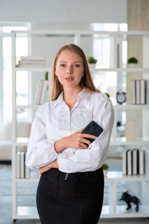 Foto de Retrato de mujer de negocios con teléfono en la mano, mirando a la cámara en el fondo borroso de la oficina. Concepto de conexión y red - Imagen libre de derechos