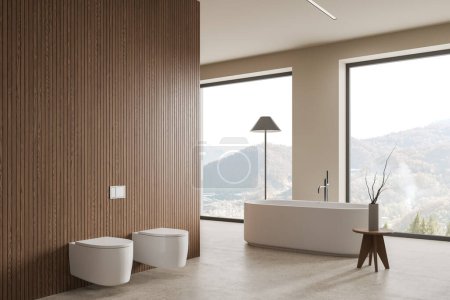 Téléchargez les photos : Intérieur de salle de bain moderne avec murs blancs et en bois, sol en béton, baignoire blanche confortable debout près de la grande fenêtre, toilettes blanches et bidet. Rendu 3d - en image libre de droit