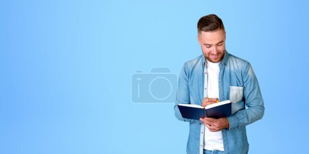 Téléchargez les photos : Jeune homme d'affaires étudiant prenant des notes dans un carnet, souriant portrait sur copie espace fond bleu. Concept d'éducation en ligne, idée d'entreprise et démarrage - en image libre de droit