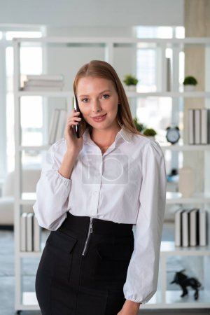 Photo for Smiling businesswoman talking on smartphone, blurred office room background. Concept of mobile app and business communication - Royalty Free Image